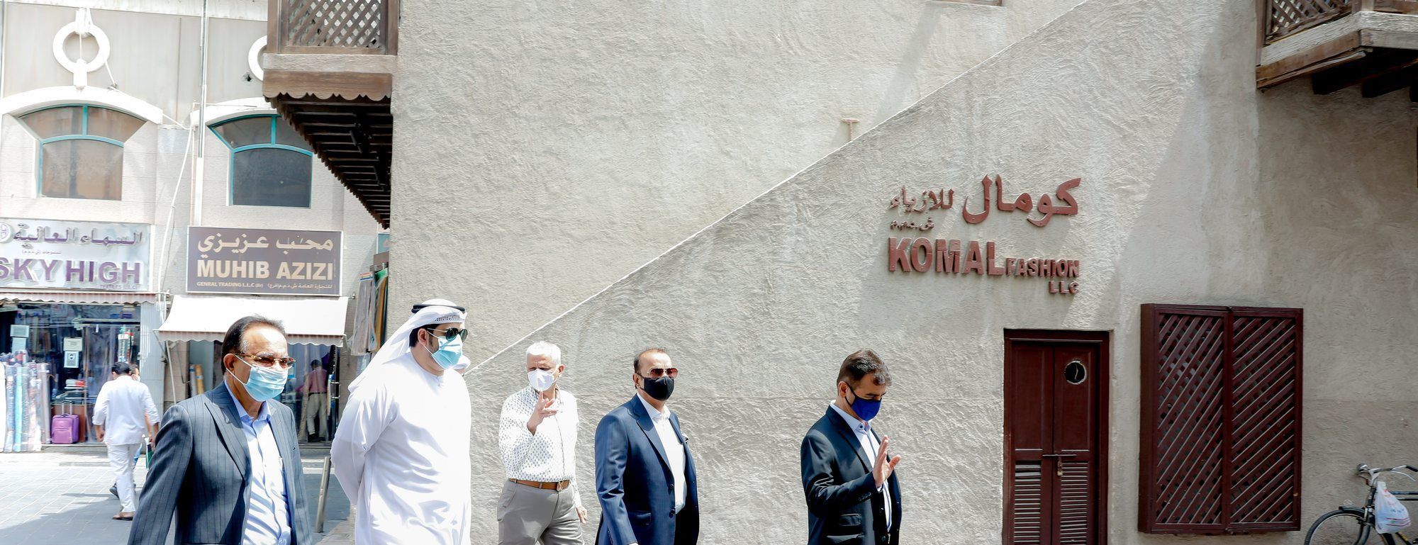 A delegation walking through the Bur Dubai textile quarter past Komal Fashion and a restored coral-stone house