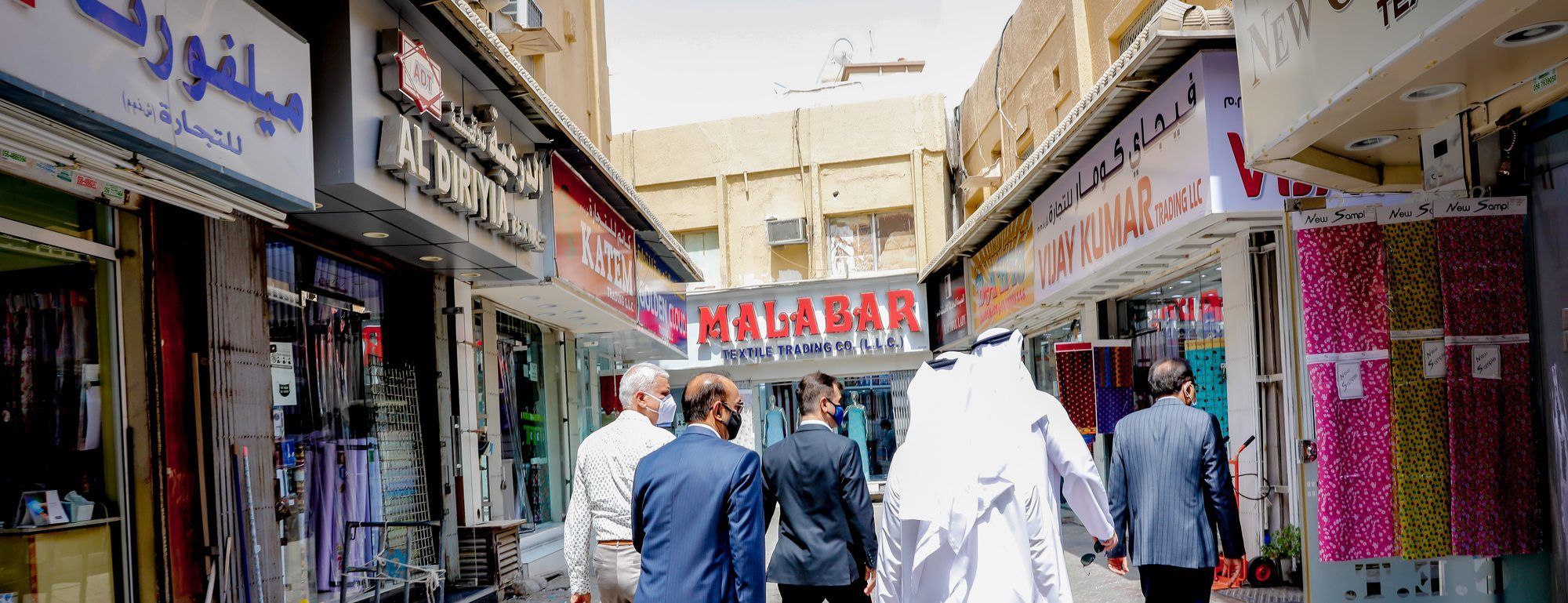 A lane of the Bur Dubai textile souq lined with member firms' shopfronts, including Malabar Textile Trading and Vijay Kumar Trading