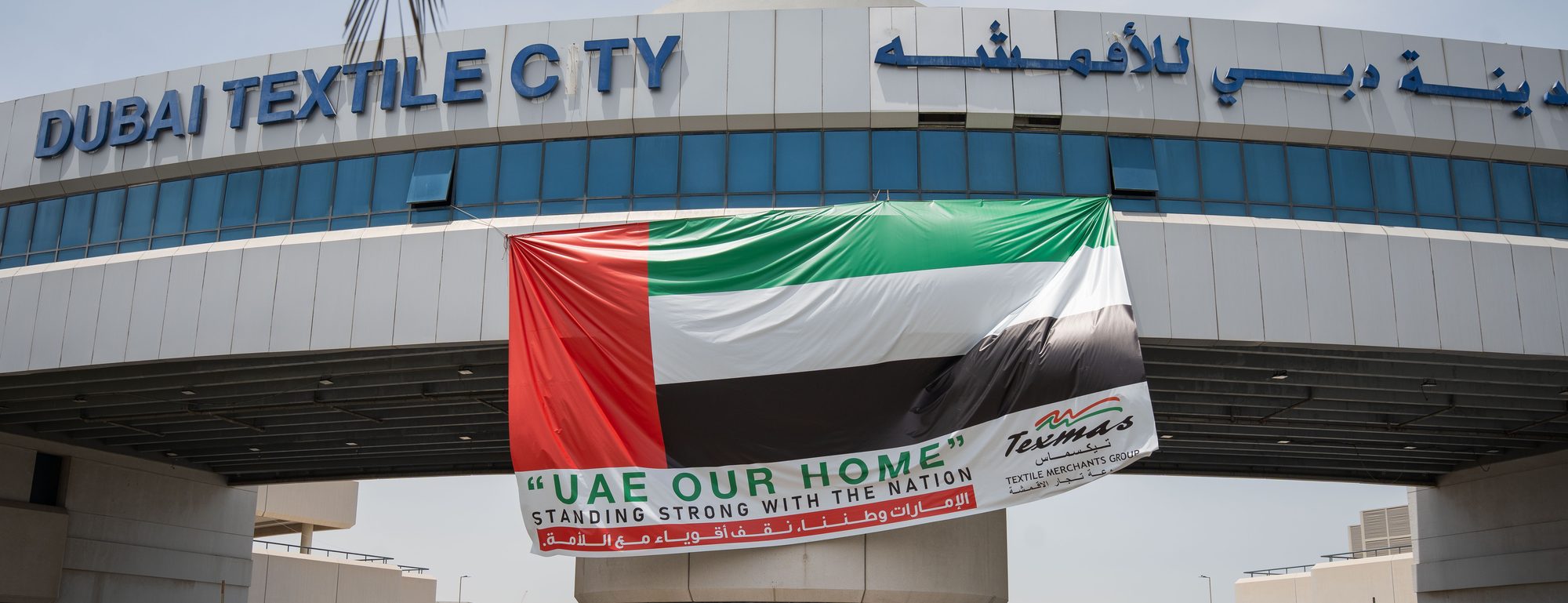 The entrance to Dubai Textile City, with a TEXMAS “UAE Our Home” banner and the UAE flag across the gate